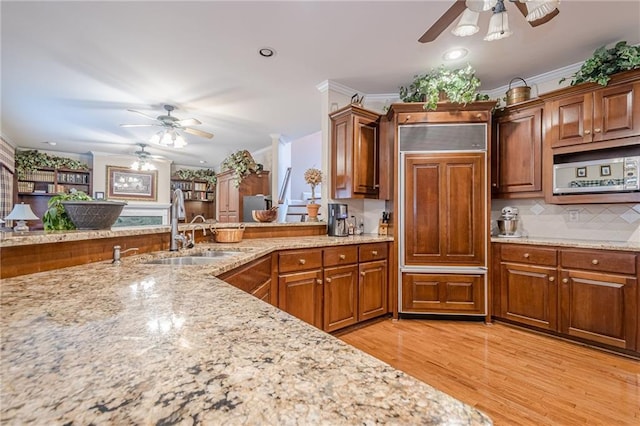 kitchen featuring paneled fridge, light wood-type flooring, a sink, crown molding, and light stone countertops