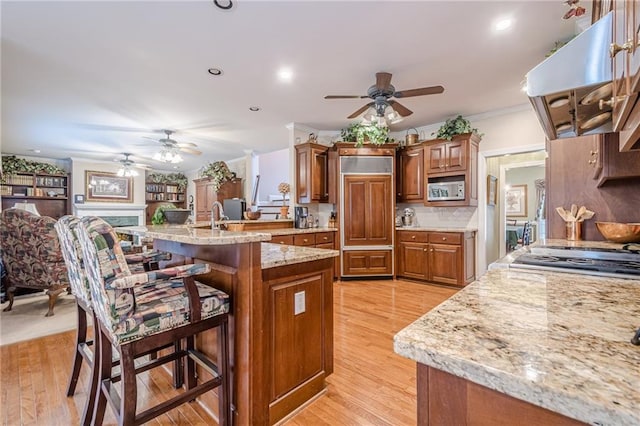 kitchen featuring brown cabinetry, light wood-style floors, under cabinet range hood, crown molding, and a kitchen breakfast bar