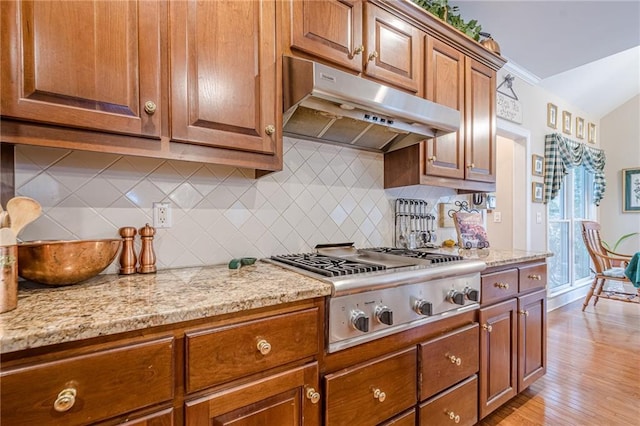 kitchen featuring under cabinet range hood, backsplash, light wood-style floors, stainless steel gas stovetop, and brown cabinetry