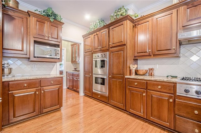 kitchen with light wood-type flooring, appliances with stainless steel finishes, ornamental molding, and brown cabinetry