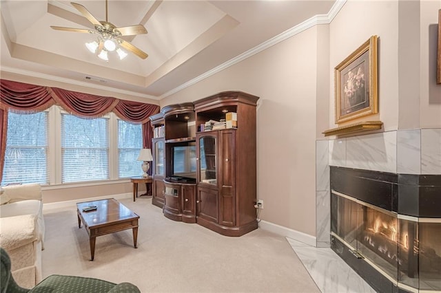 living area with crown molding, ceiling fan, baseboards, a premium fireplace, and a raised ceiling