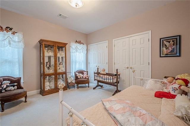 bedroom with light colored carpet, visible vents, two closets, and baseboards