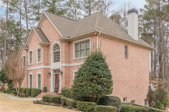 view of property exterior with a shingled roof, brick siding, and a chimney