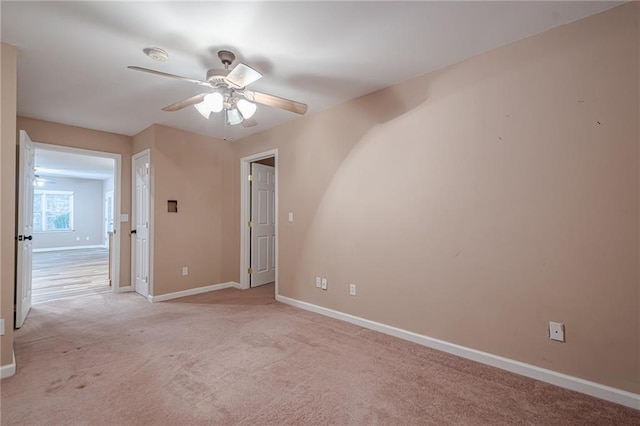 spare room with light carpet, a ceiling fan, and baseboards