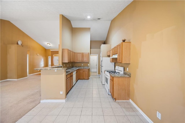 kitchen featuring lofted ceiling, white appliances, light stone countertops, light colored carpet, and kitchen peninsula