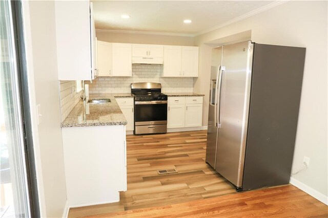 kitchen featuring white cabinets, appliances with stainless steel finishes, light stone counters, light hardwood / wood-style floors, and ornamental molding