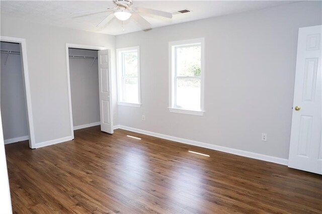 unfurnished bedroom with dark hardwood / wood-style flooring, two closets, and ceiling fan