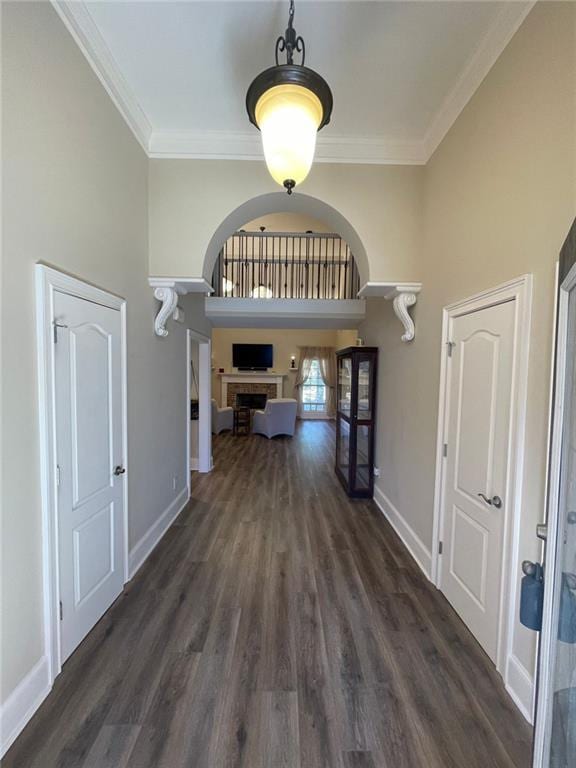 hall with wood finished floors, baseboards, arched walkways, and ornamental molding