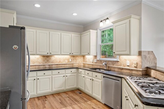 kitchen featuring crown molding, light hardwood / wood-style flooring, appliances with stainless steel finishes, decorative backsplash, and sink