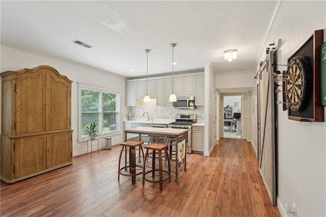 3235 Munsey Ct, Cumming, GA 30041 - kitchen with stainless steel appliances, a barn door, light countertops, light wood finished floors, and ornamental molding