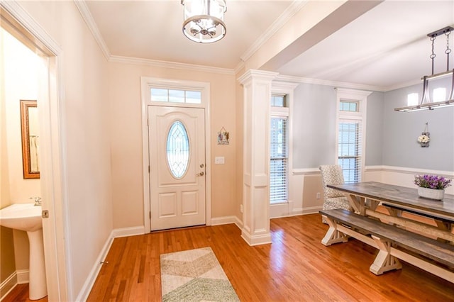 foyer entrance featuring a chandelier, baseboards, light wood-style floors, ornamental molding, and ornate columns