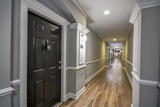 hallway featuring arched walkways, wood finished floors, baseboards, ornamental molding, and ornate columns