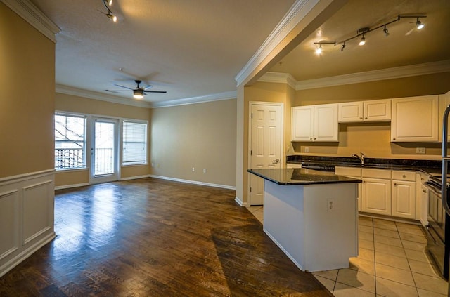 kitchen featuring a ceiling fan, a kitchen island, ornamental molding, white cabinetry, and a sink