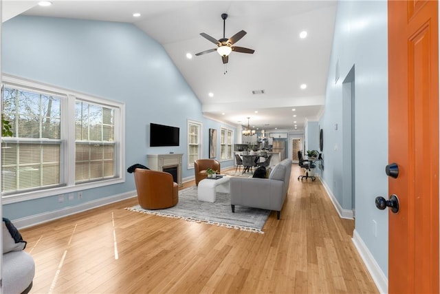 living area featuring baseboards, a fireplace, light wood-style floors, and high vaulted ceiling