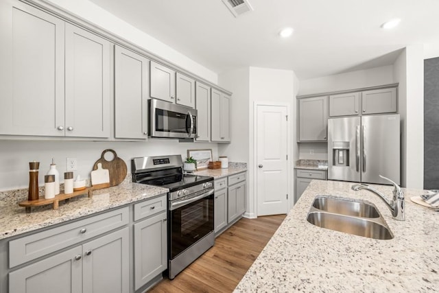 kitchen featuring light stone countertops, sink, light hardwood / wood-style flooring, and appliances with stainless steel finishes