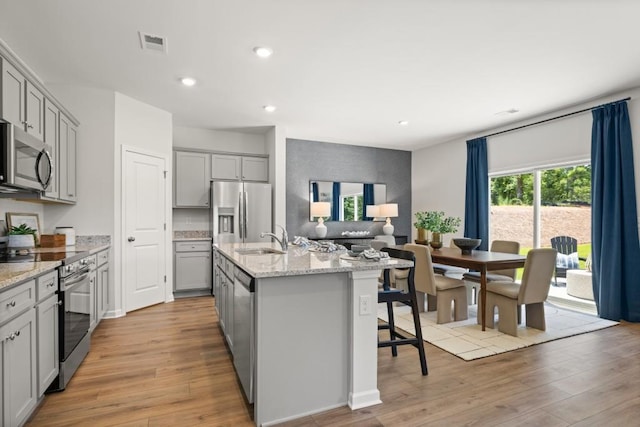 kitchen featuring gray cabinets, light hardwood / wood-style floors, stainless steel appliances, and an island with sink