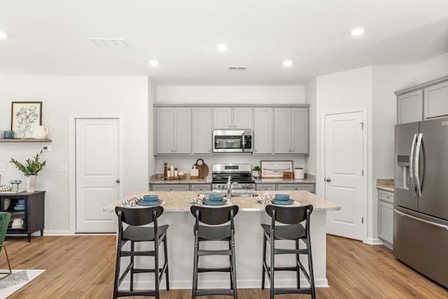 kitchen with stainless steel appliances, light hardwood / wood-style flooring, and an island with sink