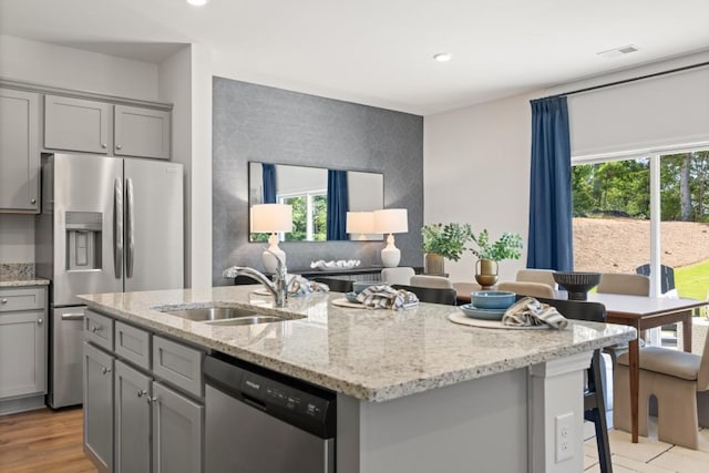 kitchen with light stone countertops, a kitchen bar, stainless steel appliances, sink, and an island with sink