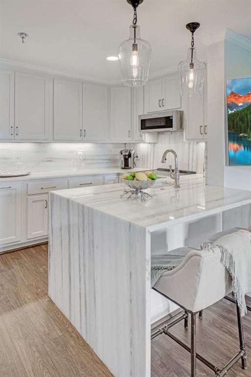 300 Johnson Ferry Rd NE Unit A706, Atlanta, GA 30328 - kitchen featuring light stone countertops, light wood finished floors, white cabinets, hanging light fixtures, and a breakfast bar
