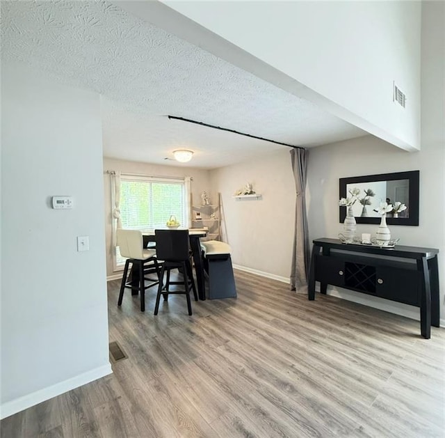 dining area featuring a textured ceiling, baseboards, visible vents, and wood finished floors