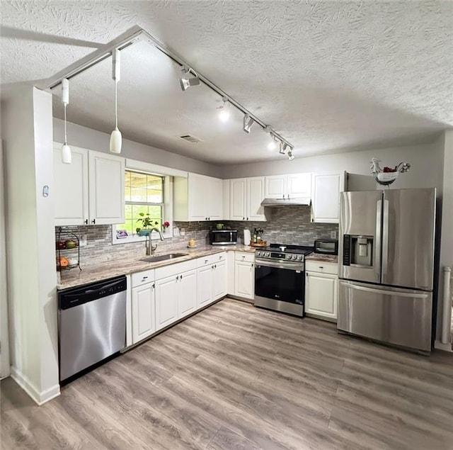 kitchen with wood finished floors, white cabinets, a sink, backsplash, and stainless steel appliances