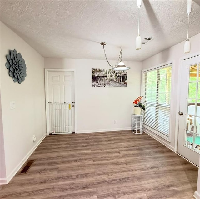 unfurnished dining area featuring a textured ceiling, baseboards, wood finished floors, and visible vents