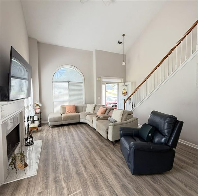 living area with a high end fireplace, wood finished floors, baseboards, a high ceiling, and stairs
