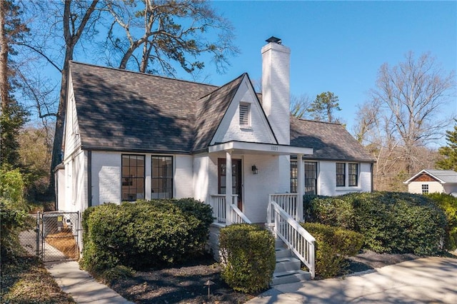 view of front of house with a shingled roof, a gate, brick siding, and a chimney