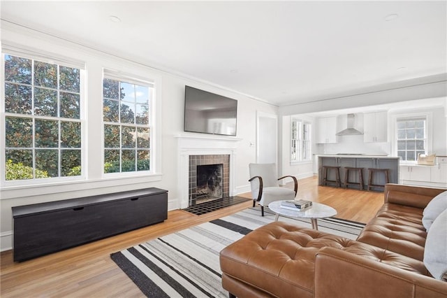 living room with light wood finished floors, a tiled fireplace, and baseboards