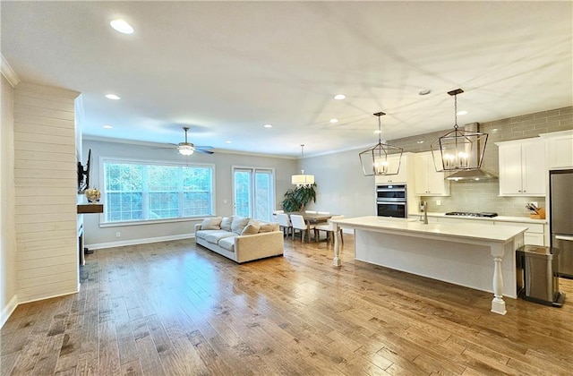 interior space with ornamental molding, decorative light fixtures, hardwood / wood-style floors, a kitchen island with sink, and wall chimney range hood