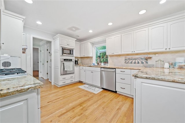 kitchen with stainless steel appliances, white cabinets, light wood-style flooring, light stone countertops, and backsplash