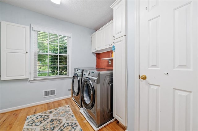 washroom with washing machine and dryer, cabinet space, light wood-style flooring, a textured ceiling, and baseboards