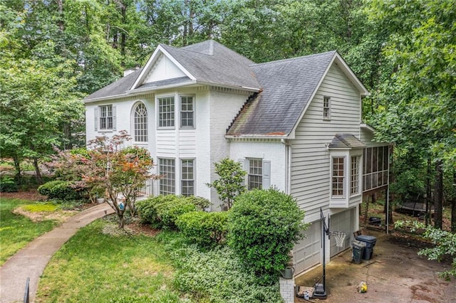 view of front of property with a garage, roof with shingles, brick siding, view of wooded area, and concrete driveway