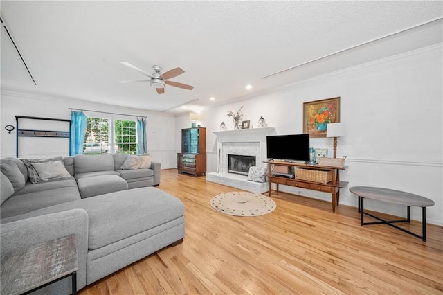 living area with ceiling fan, crown molding, light wood-style flooring, a fireplace with raised hearth, and recessed lighting