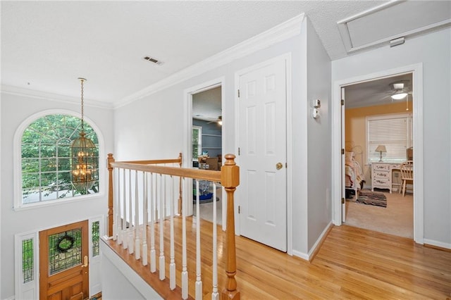 corridor featuring an upstairs landing, light wood finished floors, baseboards, ornamental molding, and a chandelier