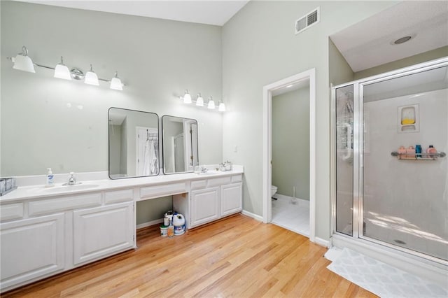 bathroom featuring double vanity, a stall shower, and wood finished floors