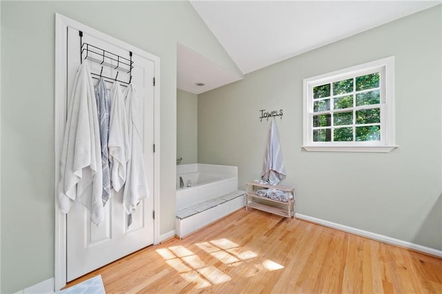 full bath featuring vaulted ceiling, a bath, wood finished floors, and baseboards
