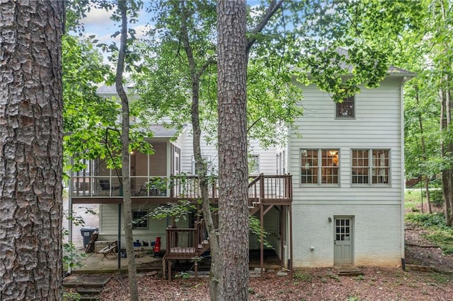 rear view of house with a deck, brick siding, a sunroom, stairway, and a patio