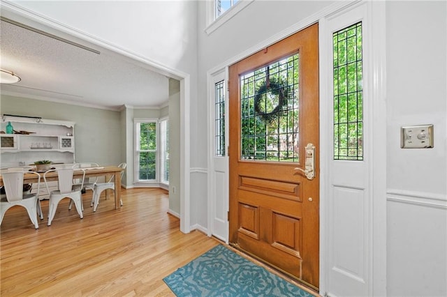 foyer featuring light wood-style flooring, ornamental molding, and a textured ceiling