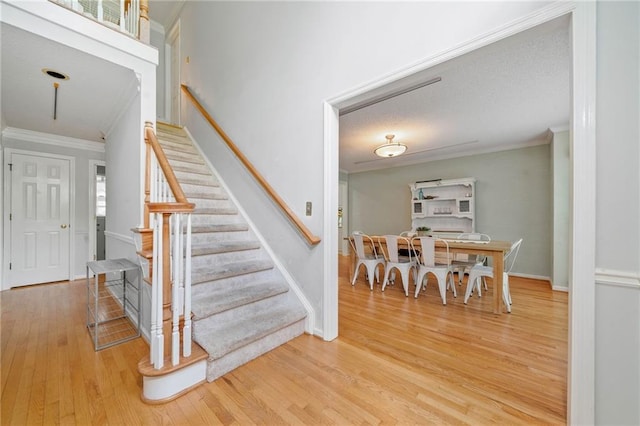 staircase with crown molding, wood finished floors, and baseboards