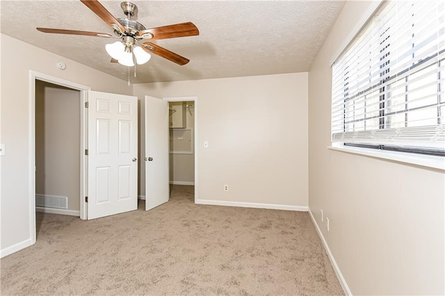 unfurnished bedroom with a walk in closet, ceiling fan, a textured ceiling, light colored carpet, and a closet