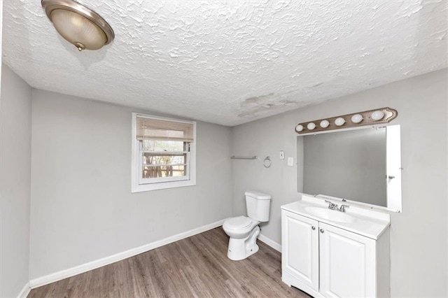 bathroom with baseboards, toilet, vanity, wood finished floors, and a textured ceiling