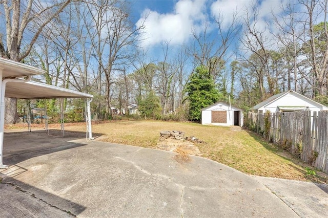 view of yard with fence, driveway, an outdoor structure, a carport, and a storage shed