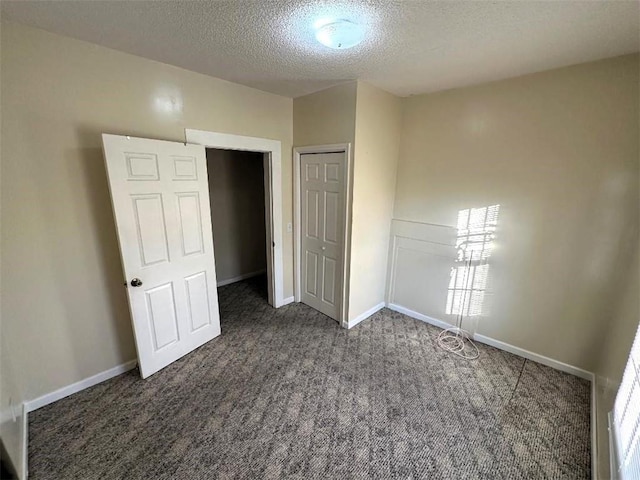 unfurnished bedroom featuring a textured ceiling, dark carpet, and a closet