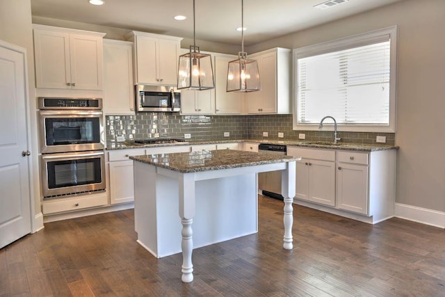 kitchen featuring dark stone counters, sink, appliances with stainless steel finishes, decorative light fixtures, and a kitchen island