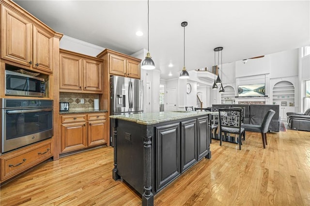 kitchen with light wood finished floors, a kitchen island, open floor plan, light stone counters, and appliances with stainless steel finishes