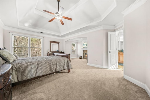 bedroom featuring a raised ceiling, ornamental molding, arched walkways, baseboards, and light colored carpet