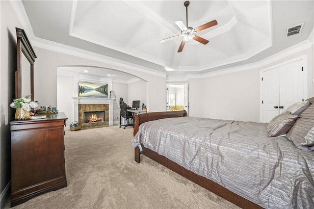 bedroom with visible vents, crown molding, carpet flooring, a raised ceiling, and a tile fireplace