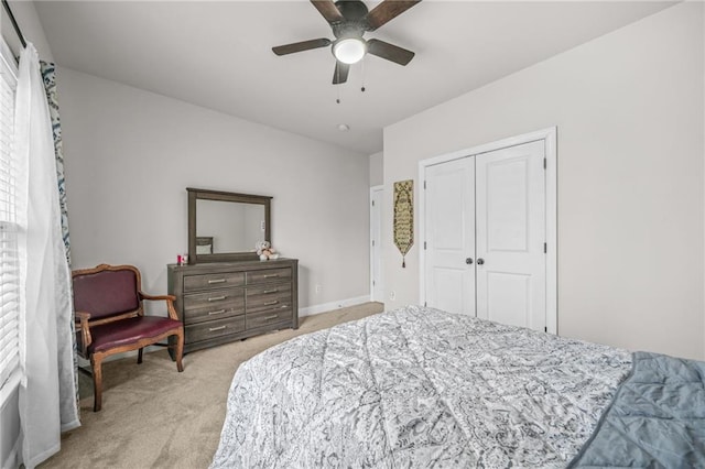 bedroom featuring a closet, light colored carpet, baseboards, and ceiling fan