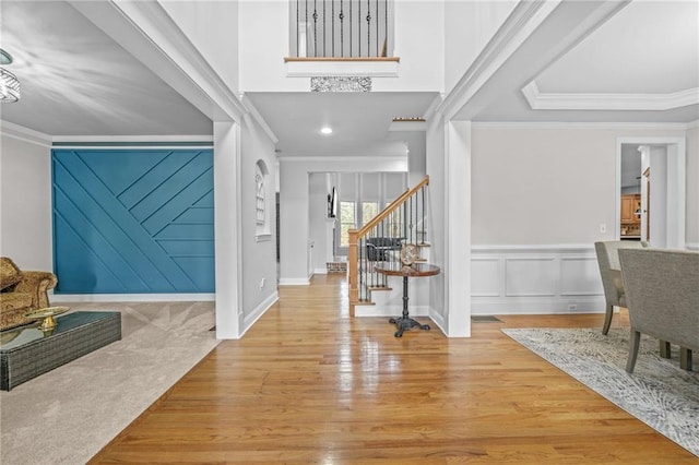 foyer entrance with stairs, a decorative wall, wood finished floors, and ornamental molding